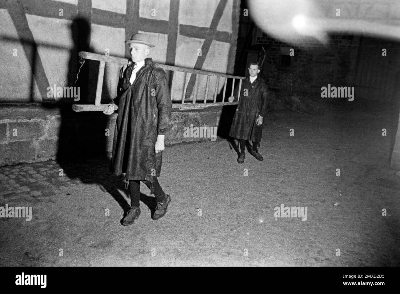 Zwei Männer in Tracht tragen eine Leiter durch das nächtliche Dorf im Schwalm-Eder-Kreis in Hessen, 1938. Due uomini in vestito tradizionale che trasportano una scala attraverso il villaggio di notte nella regione di Schwalm-Eder in Assia, 1938. Foto Stock