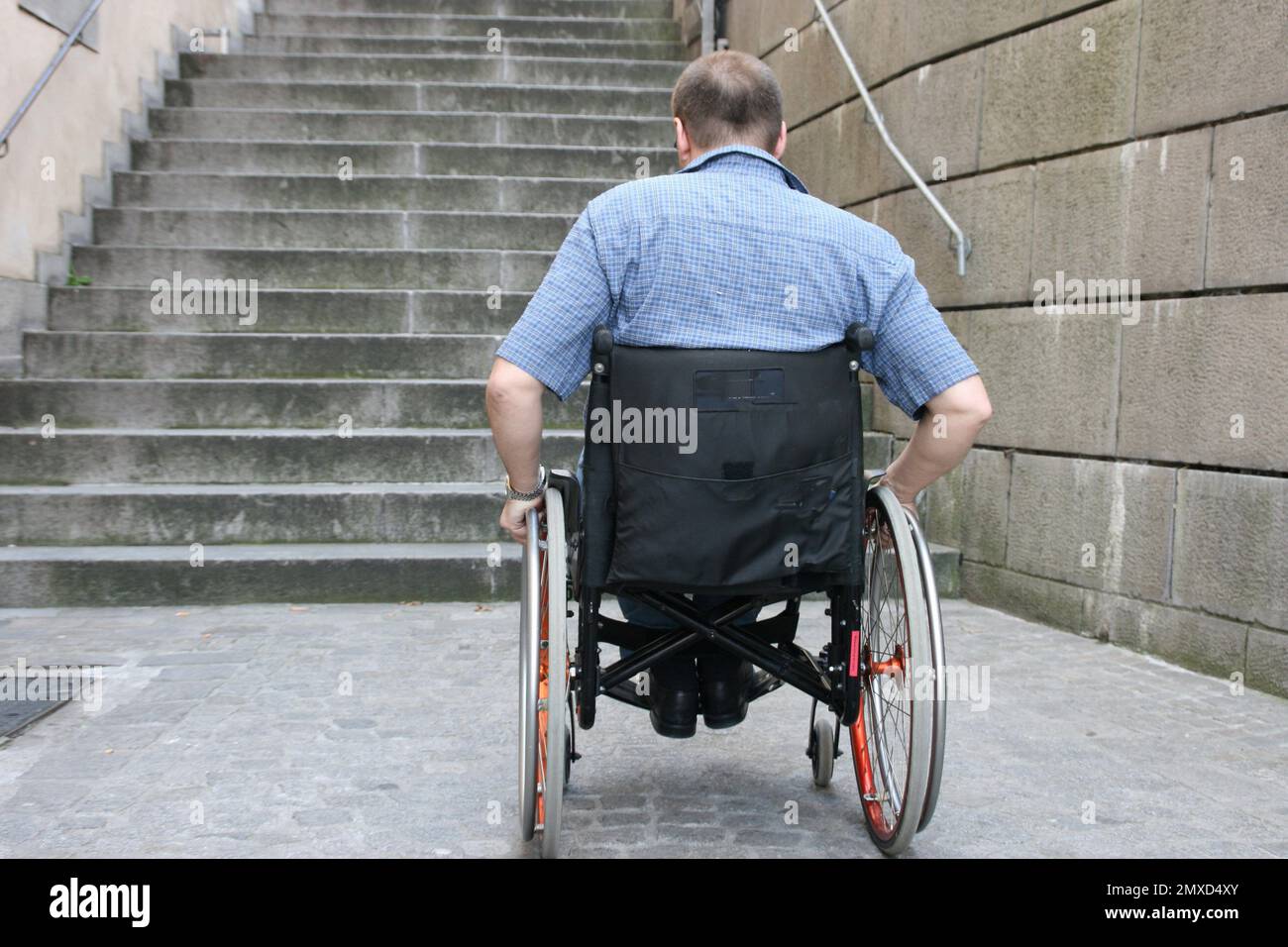 utente su sedia a rotelle in piedi di fronte a una scala esterna non priva di barriere architettoniche, vista posteriore Foto Stock