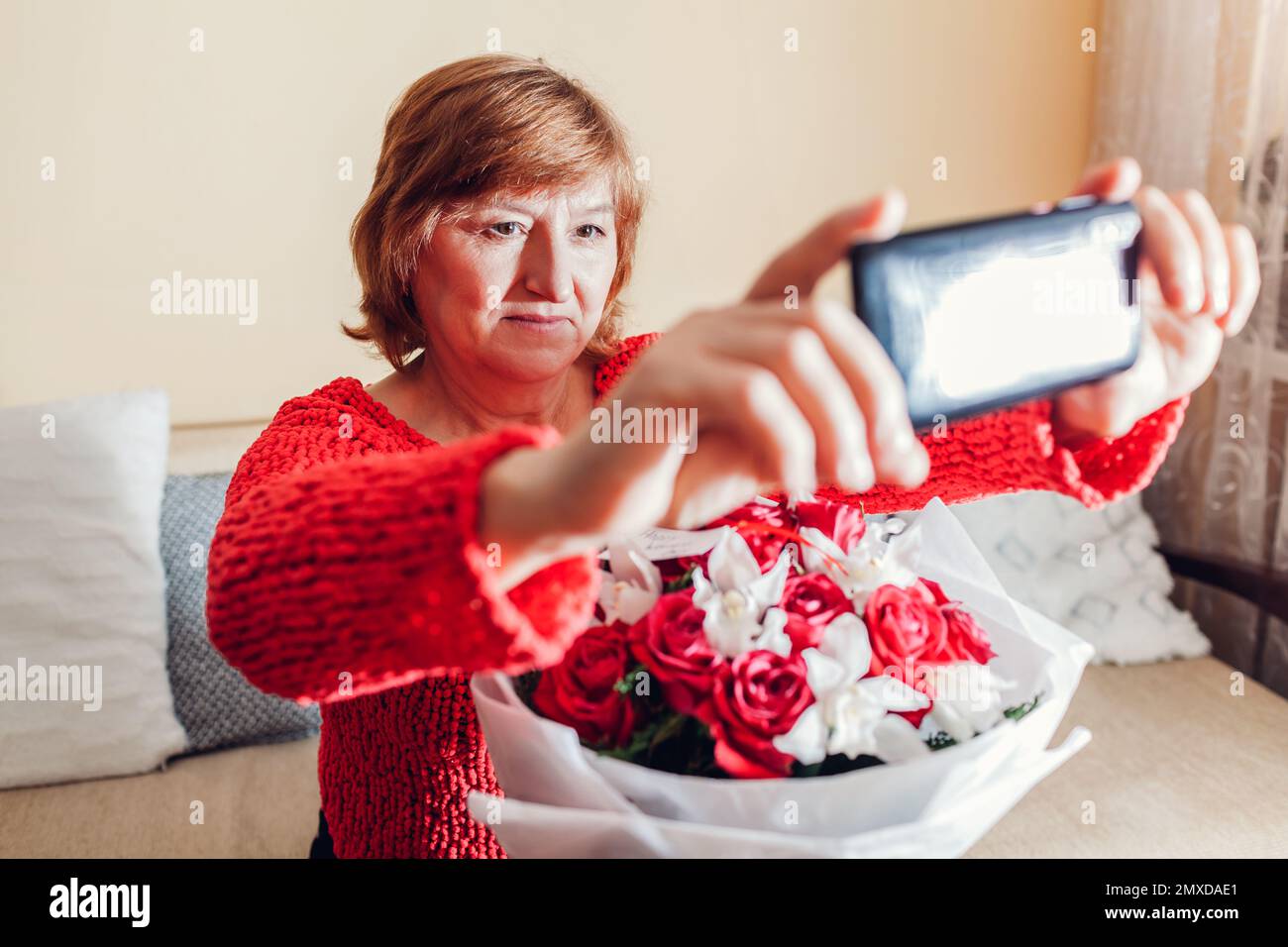 Happy Womens Day, regalo del 8 marzo. Donna anziana prende selfie con bouquet di fiori che ha trovato a casa. Sorpresa per le vacanze primaverili Foto Stock