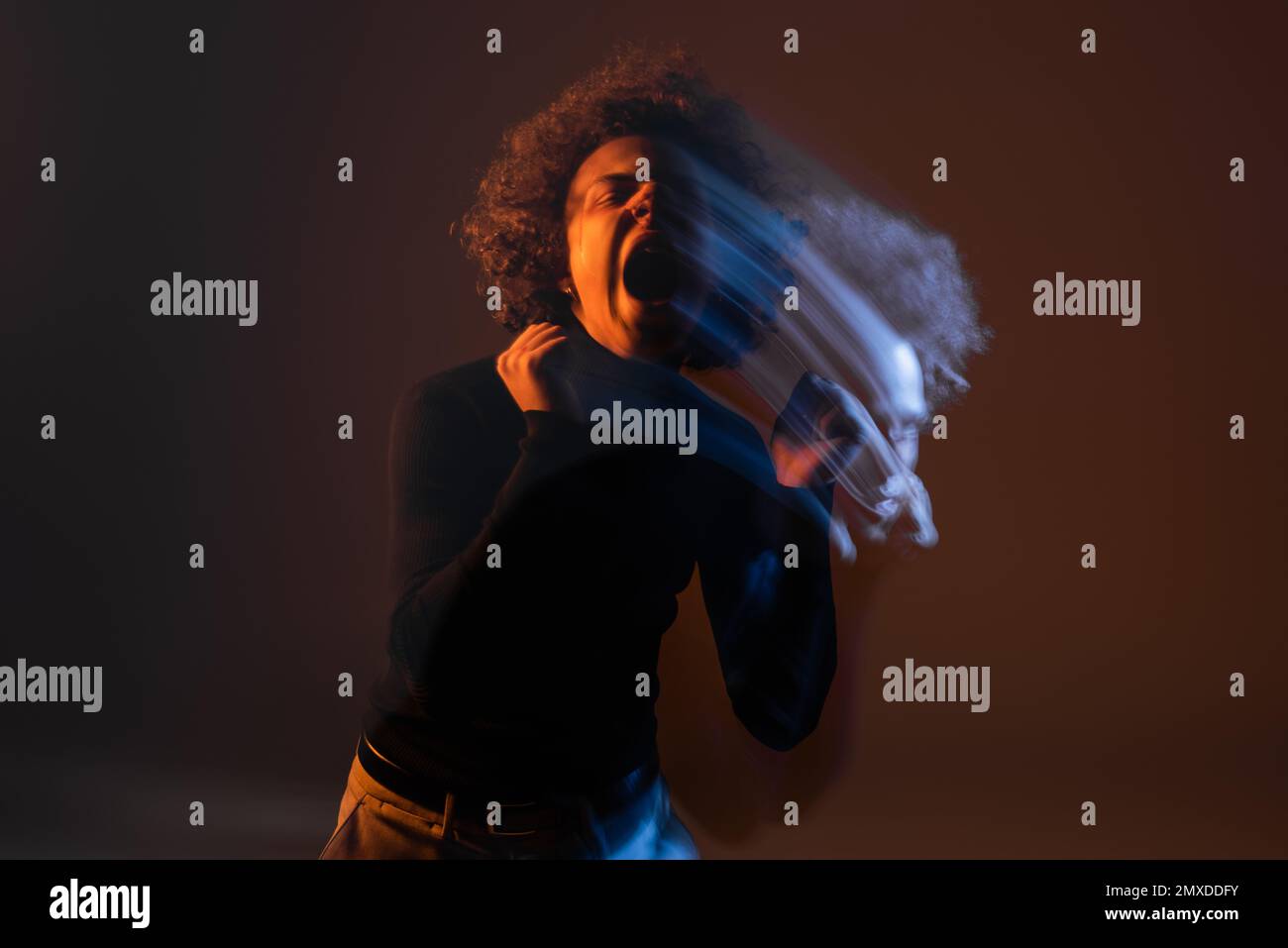 doppia esposizione di afroamericano arrabbiato con disturbo bipolare urlando su sfondo scuro con luce arancione e blu, immagine stock Foto Stock