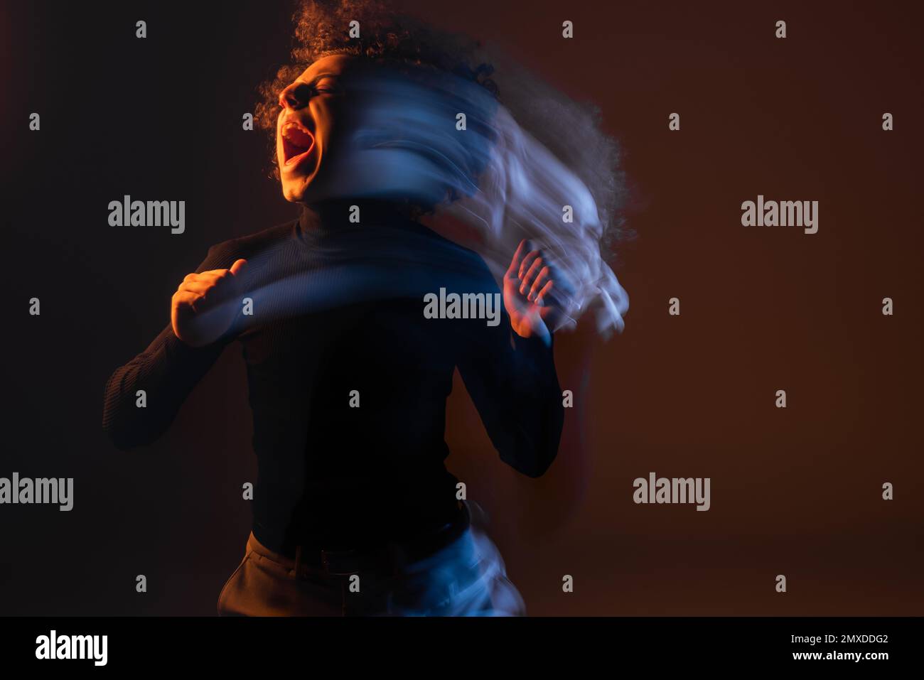 lunga esposizione di ferito e stressato afro-americano gridando su sfondo nero con luce arancione e blu, immagine stock Foto Stock