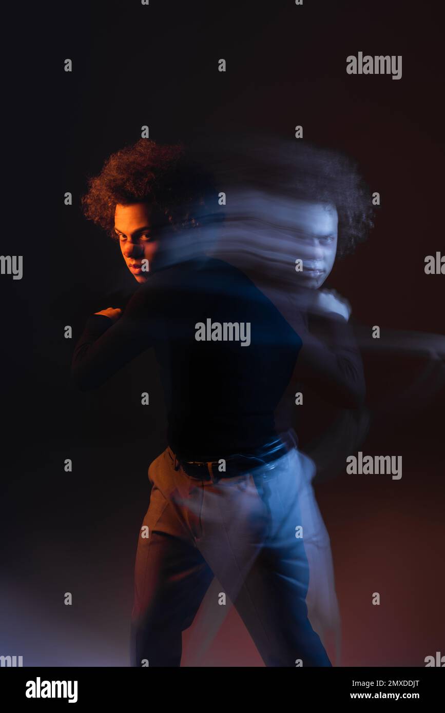 lunga esposizione di un giovane e ferito afroamericano con disturbo bipolare guardando la fotocamera in nero con luce arancione e blu, immagine stock Foto Stock