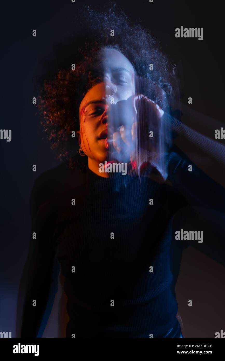 lunga esposizione di uomo afroamericano ferito con disturbo bipolare su nero con luce arancione e blu, immagine stock Foto Stock
