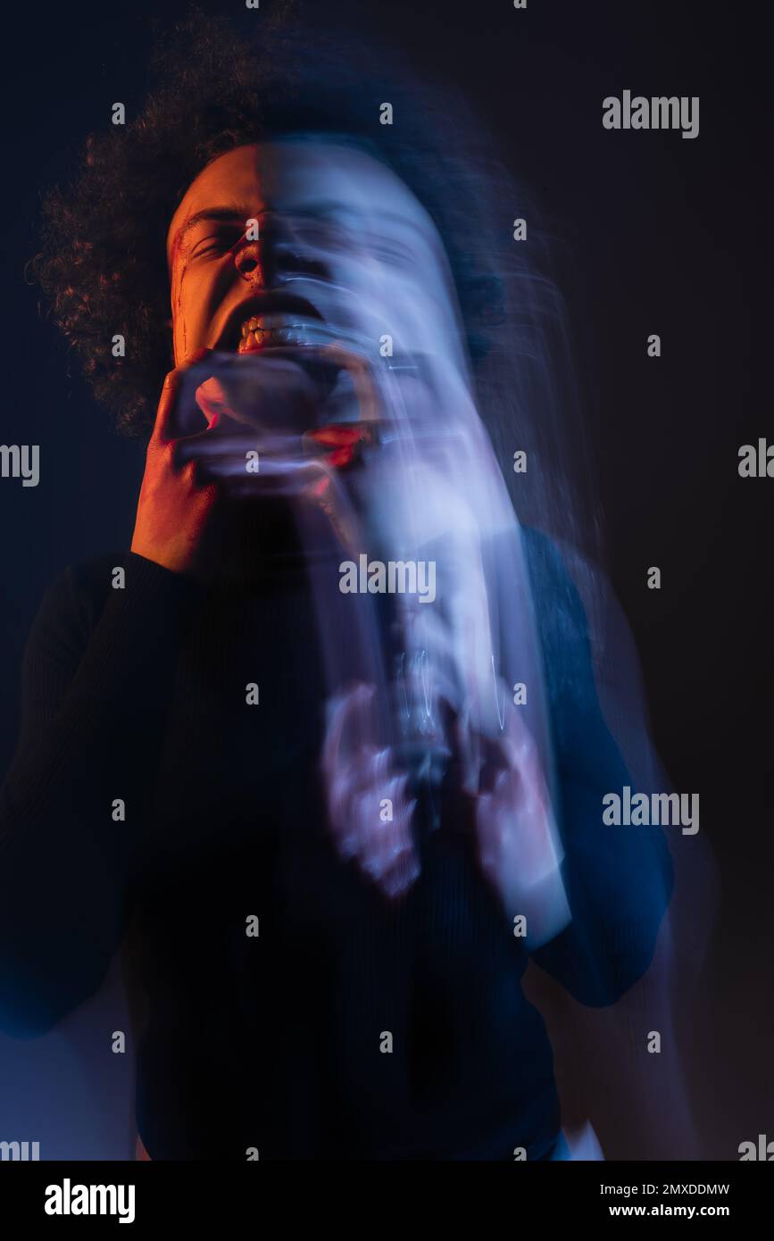lunga esposizione di uomo afroamericano ferito con disturbo bipolare e grimace arrabbiato su nero con luce arancione e blu, immagine stock Foto Stock