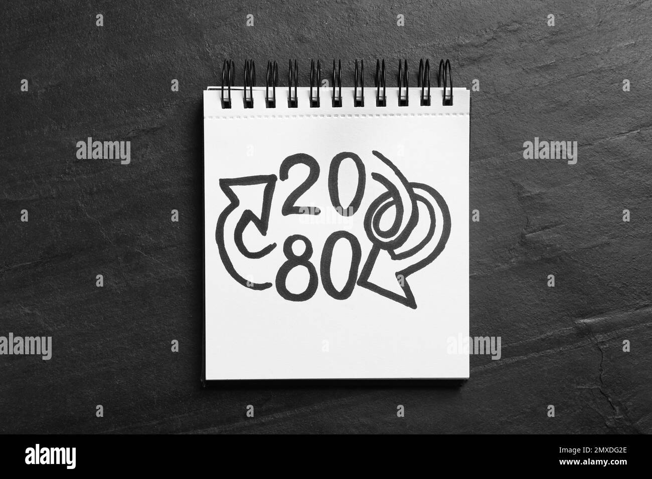 Notebook con numeri 20, 80 e frecce su sfondo nero ardesia, vista dall'alto. Principio di Pareto Foto Stock