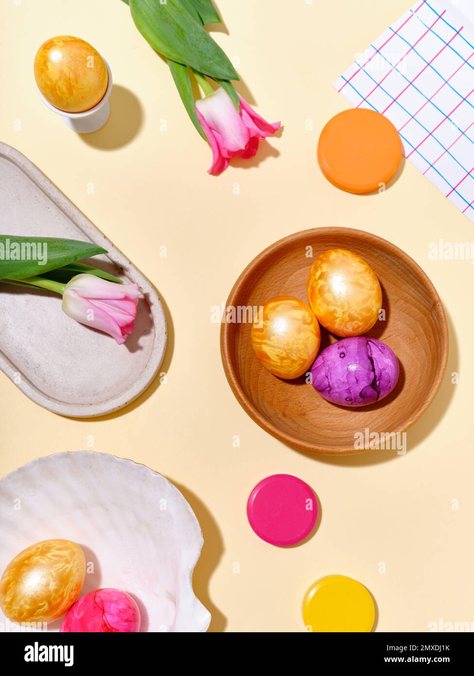 Piatto still vita con uova di pasqua colorate e tulipani rosa su sfondo giallo luminoso. Foto Stock