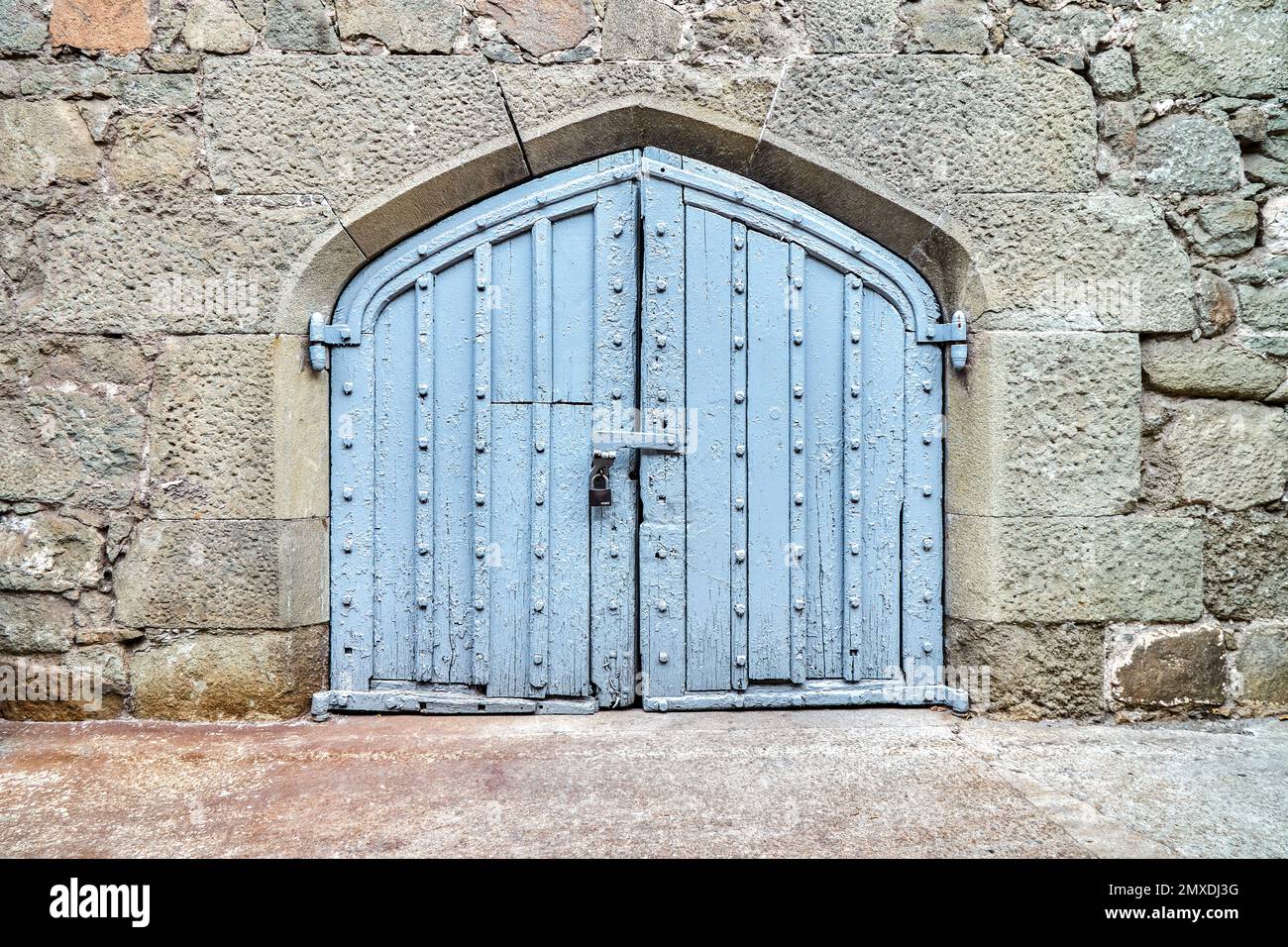 Il cancello di legno blu sulle pareti circondato da pietre in design medievale nasconde le cose misteriose dai visitatori in arrivo. Esterno del luogo medievale Foto Stock