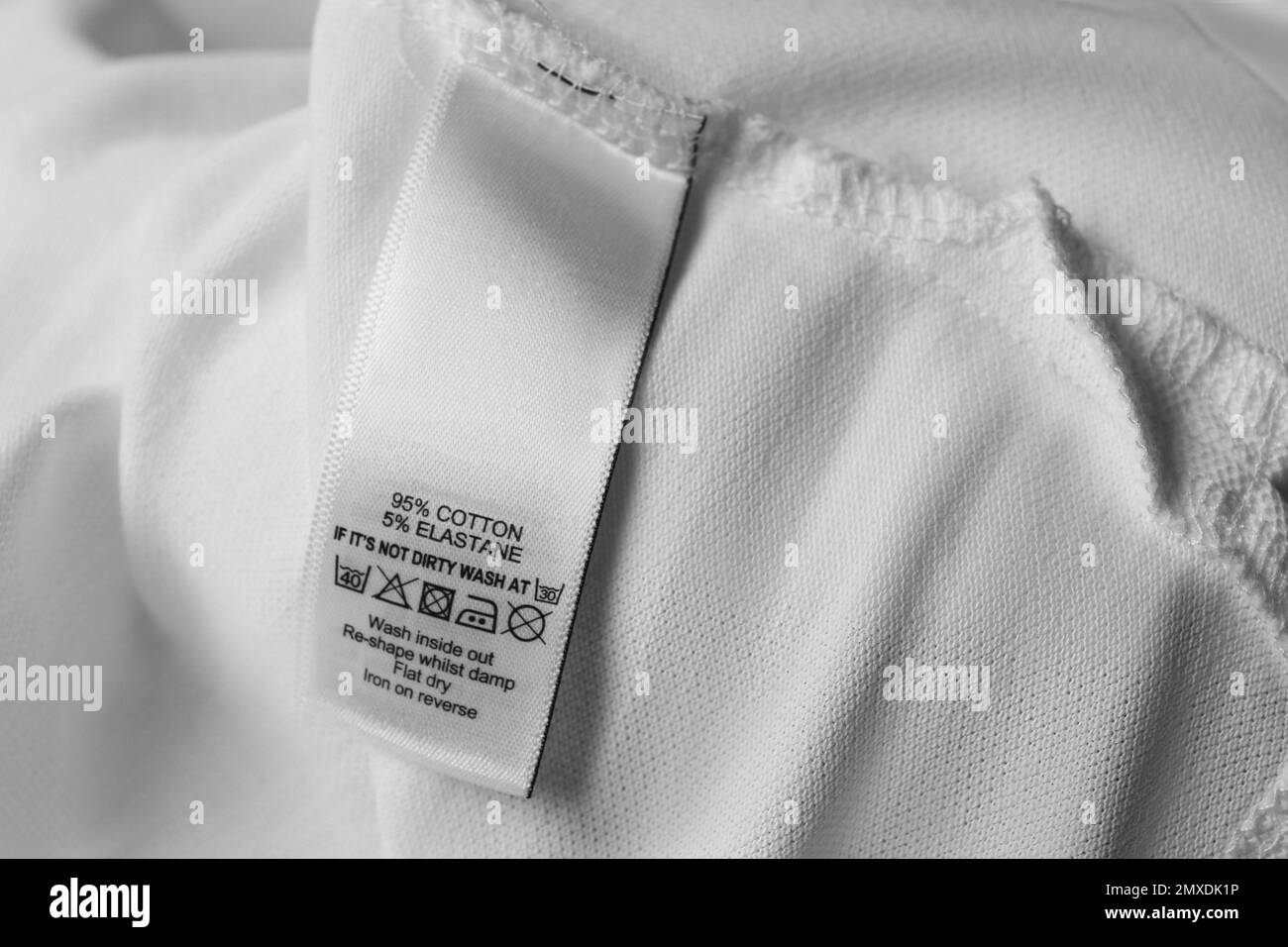 Etichetta di abbigliamento con simboli di cura e contenuto del materiale su camicia bianca, vista primo piano Foto Stock