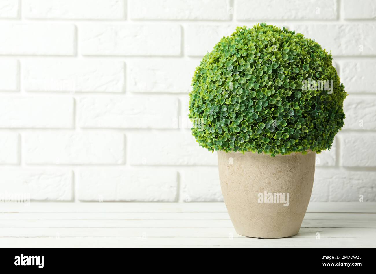 Bella pianta artificiale in vaso di fiori su tavolo di legno bianco vicino muro di mattoni. Spazio per il testo Foto Stock