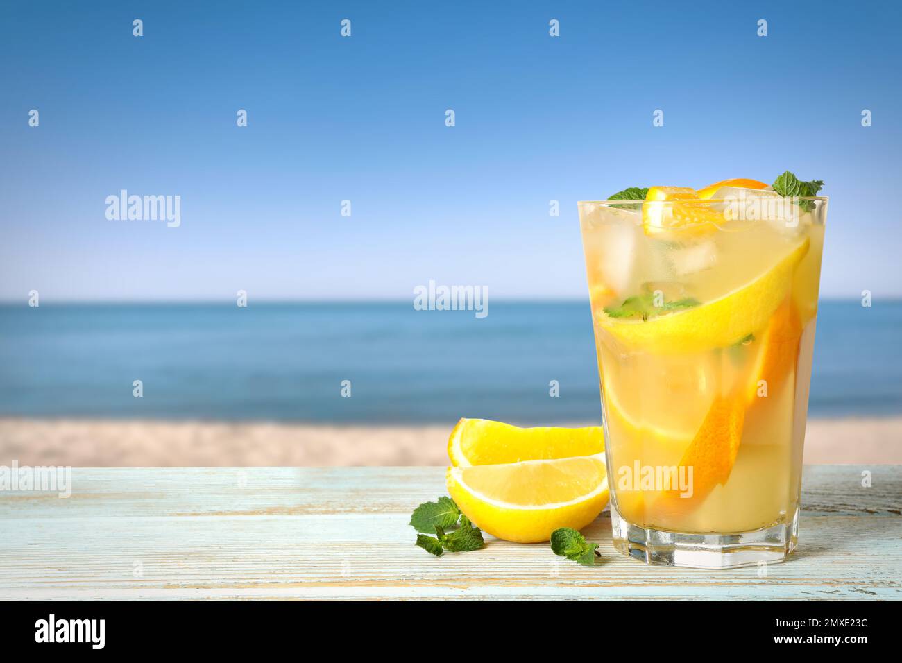 Limonata di agrumi con cubetti di ghiaccio su tavola di legno vicino al mare, spazio per il testo Foto Stock