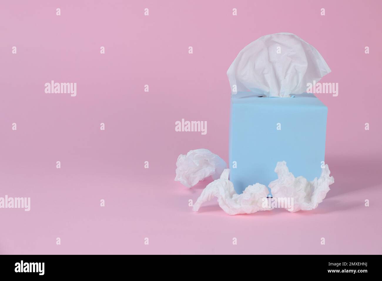 Scatola con fazzolettini di carta e tovaglioli stropicciati usati su sfondo rosa, spazio per il testo Foto Stock