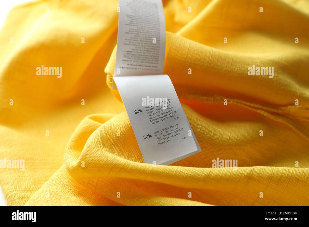 Etichetta di abbigliamento con informazioni sul contenuto su indumento giallo, primo piano Foto Stock