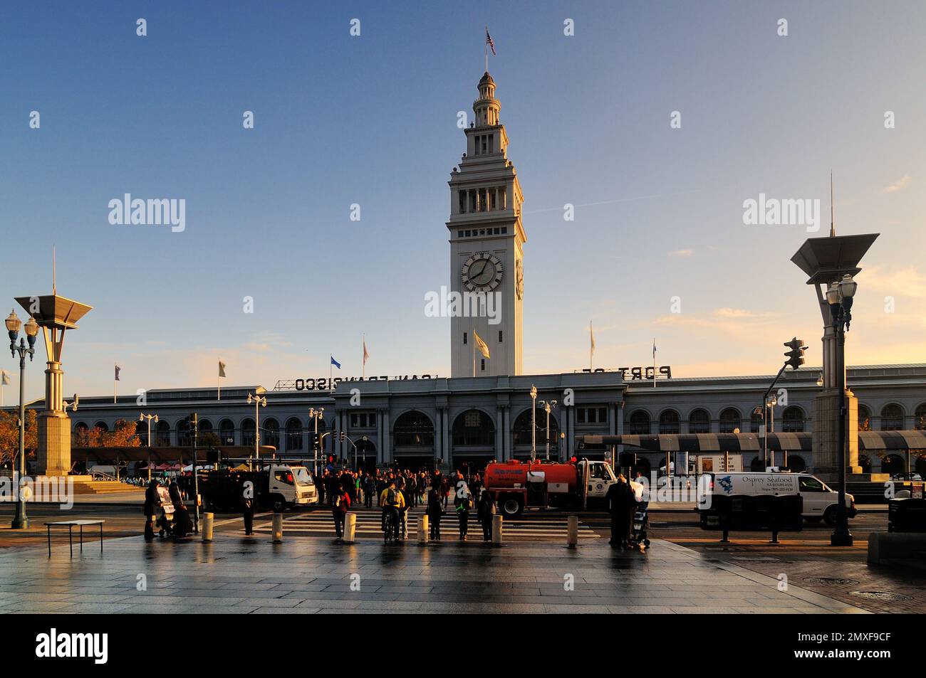 L'iconico Ferry Building di San Francisco con la sua torre dell'orologio al tramonto. La folla, i lampioni e i riflessi creano una vista panoramica in questo centro storico Foto Stock