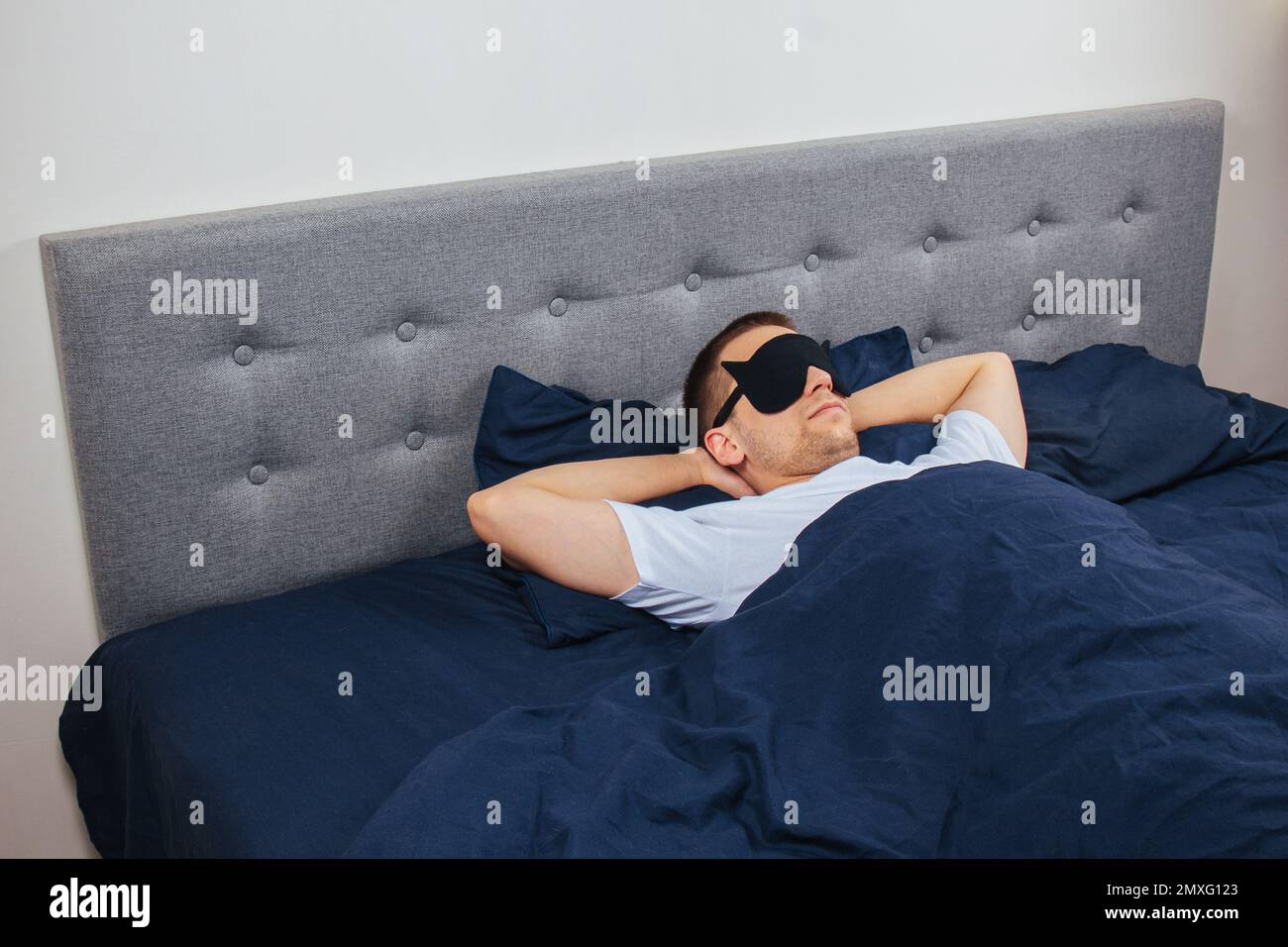 Vista dall'alto foto ad alto angolo di un giovane uomo che indossa maschera di sonno, sorriso positivo felice, coperta di sonno, coperta, vestiti, pigiami Foto Stock