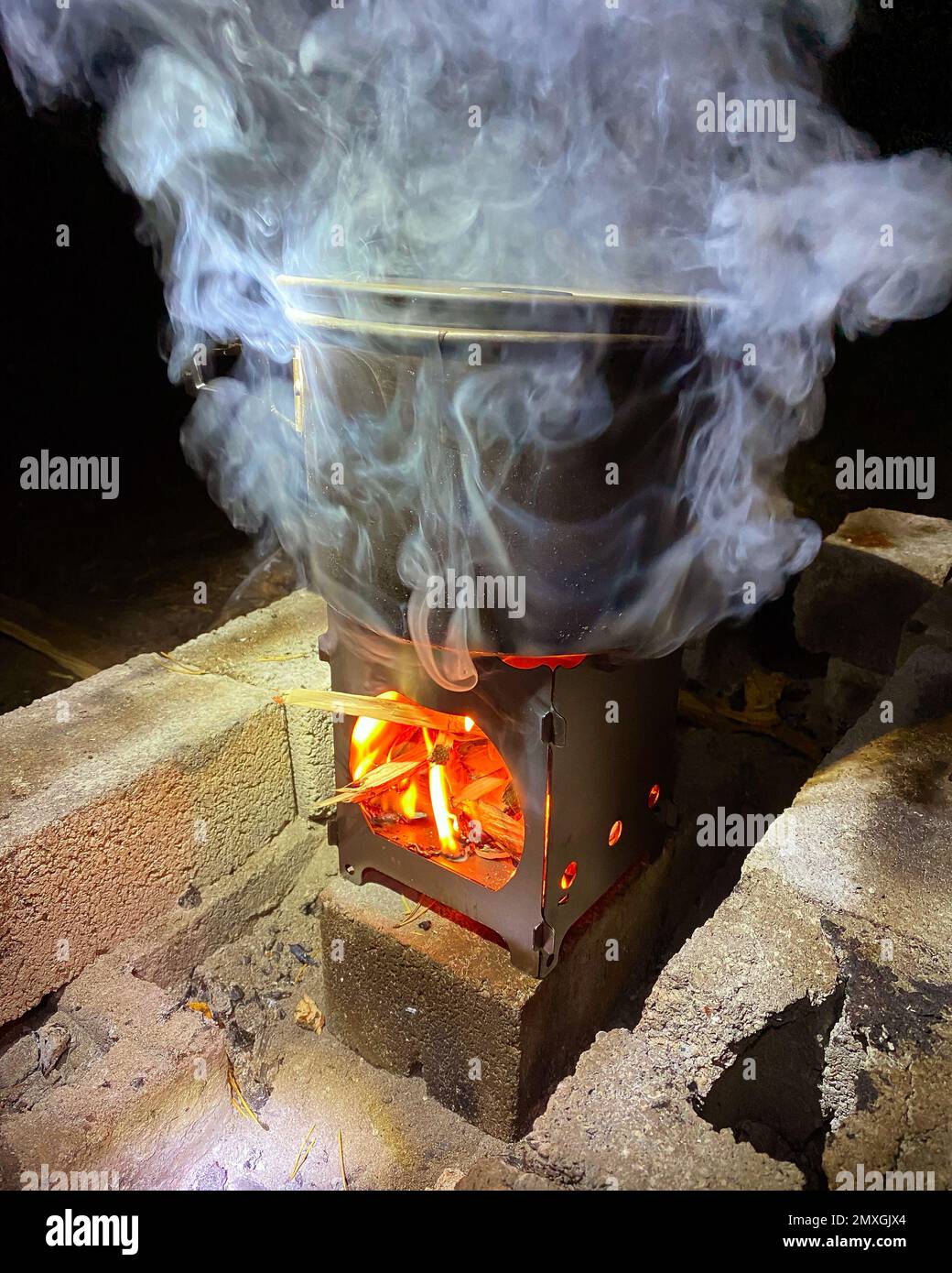 Una pentola si trova su un bruciatore a legna con fuoco e fumo. Cucina da viaggio. Foto Stock