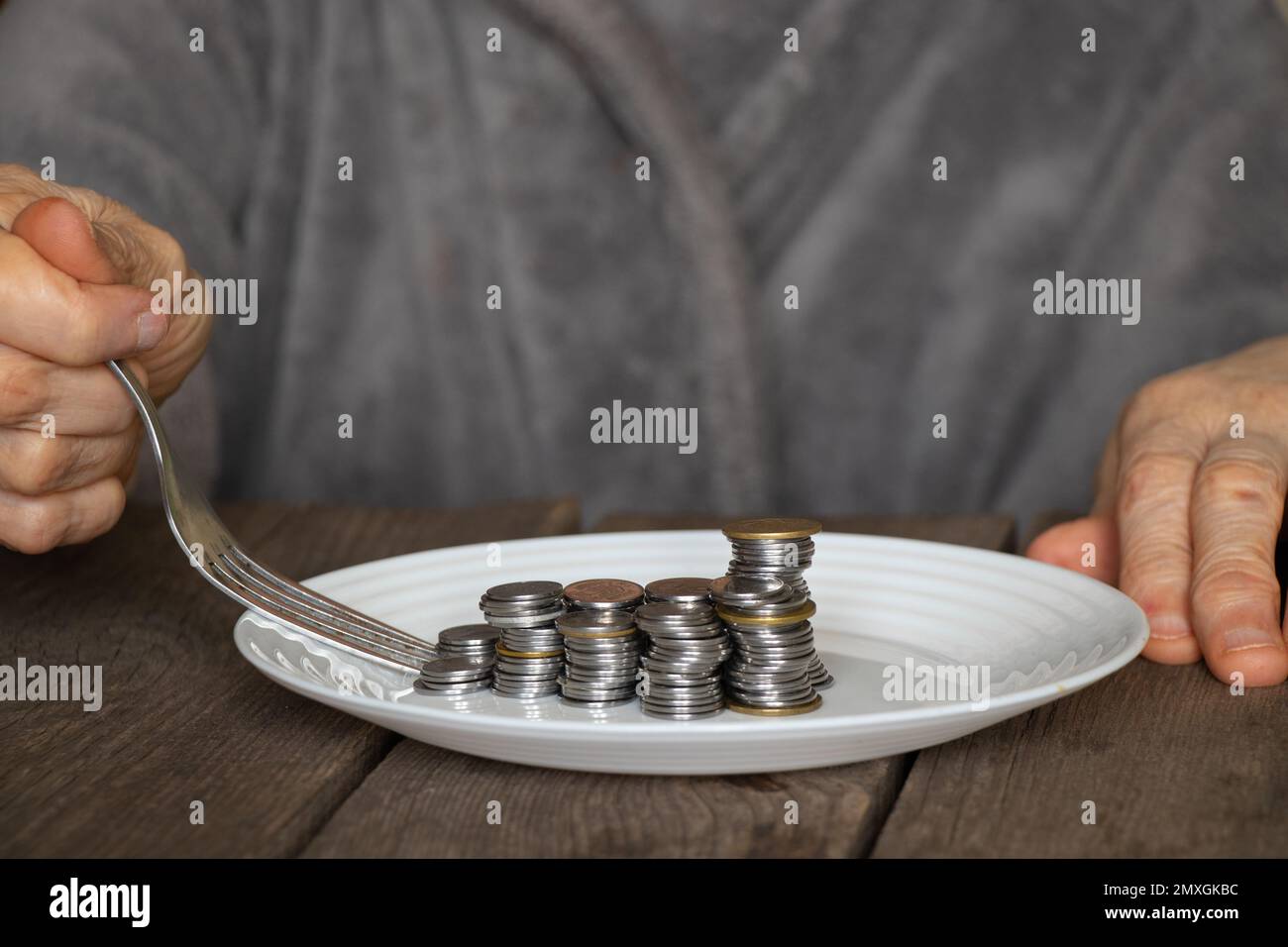 una pila di monete su un piatto bianco su un vecchio tavolo di legno e vecchie mani femminili versarono un piatto a casa in cucina Foto Stock