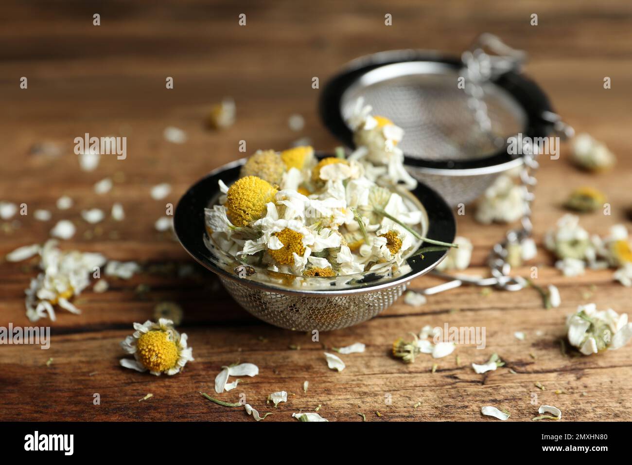 Fiori di camomilla asciutti in infusore su tavolo di legno, primo piano Foto Stock