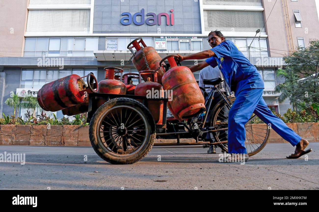 Un uomo spinge un triciclo carico di bombole di GPL sulla strada sotto il cartello Adani a Mumbai. La denuncia della società di ricerca DI HINDENBURG SULLA frode da parte DI Adani Enterprise, FONDATA NEGLI STATI UNITI, ha scatenato un dibattito politico in India da parte dei partiti dell'opposizione. Foto Stock