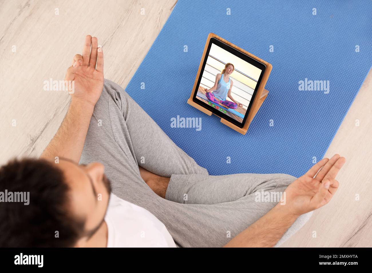 Corso di yoga a distanza durante la pandemia di coronavirus. Uomo che pratica online con l'insegnante tramite tablet a casa, vista dall'alto Foto Stock