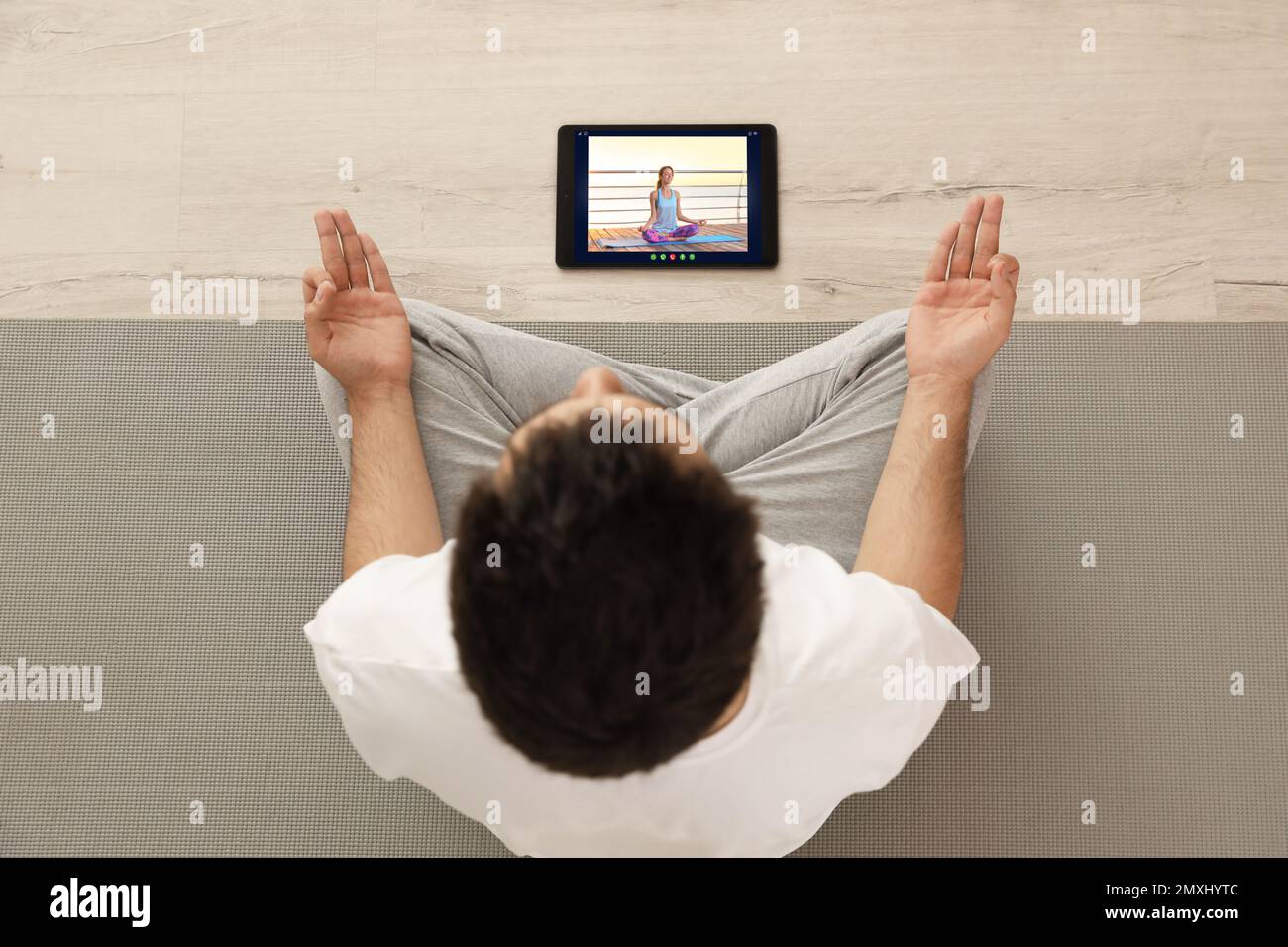 Corso di yoga a distanza durante la pandemia di coronavirus. Uomo che pratica online con l'insegnante tramite tablet a casa, vista dall'alto Foto Stock