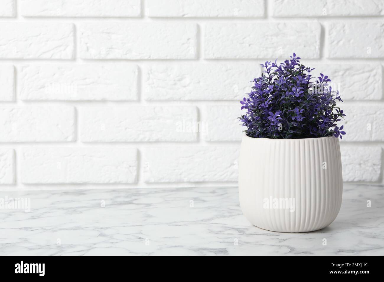 Bella pianta artificiale in vaso di fiori su tavolo di marmo bianco vicino a muro di mattoni. Spazio per il testo Foto Stock