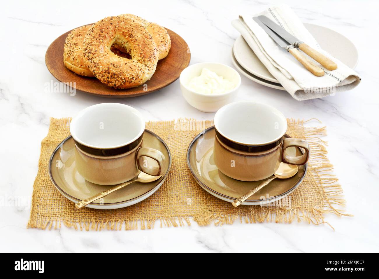 Bagel freschi e formaggio cremoso con tazze e piattini preparati per una pausa caffè rustica in formato orizzontale e shot in luce naturale. Foto Stock