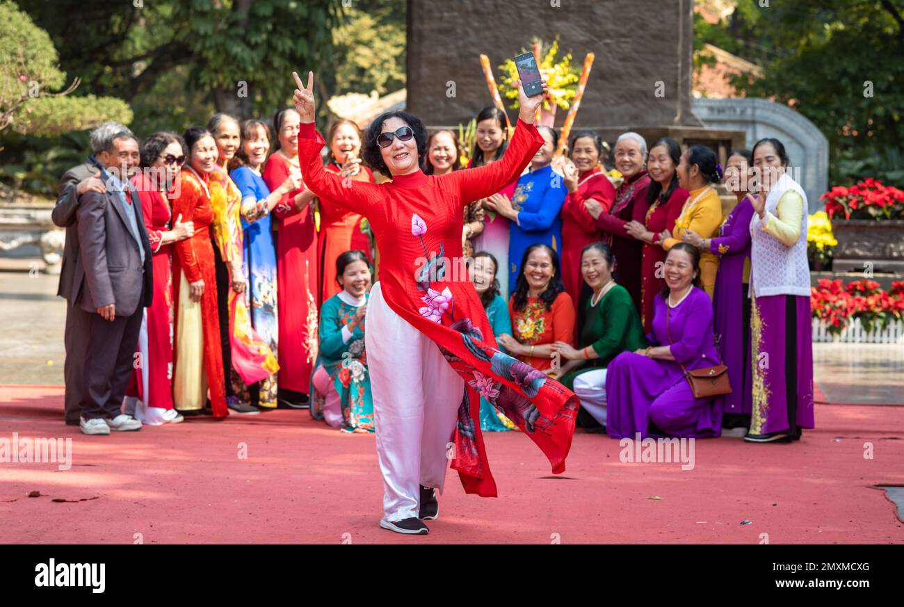 Una donna gesta come un grande gruppo di donne per lo più vietnamite vestite di colorato tradizionale ao dai, organizzarsi per posare per una foto di gruppo dentro Foto Stock
