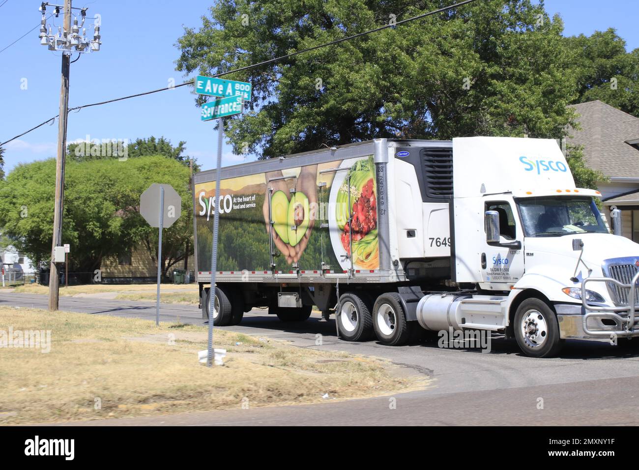 Un camion Sysco semi che consegna cibo che si ferma a un segnale di stop con alberi e cielo blu Foto Stock