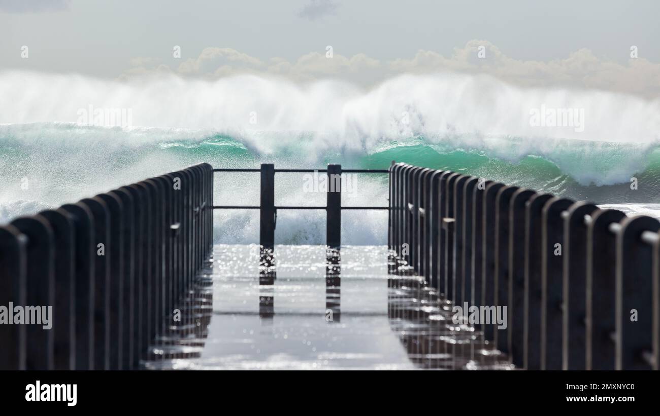 L'acqua dell'oceano che esplode davanti al molo della spiaggia, il sentiero pedonale del molo. Foto Stock