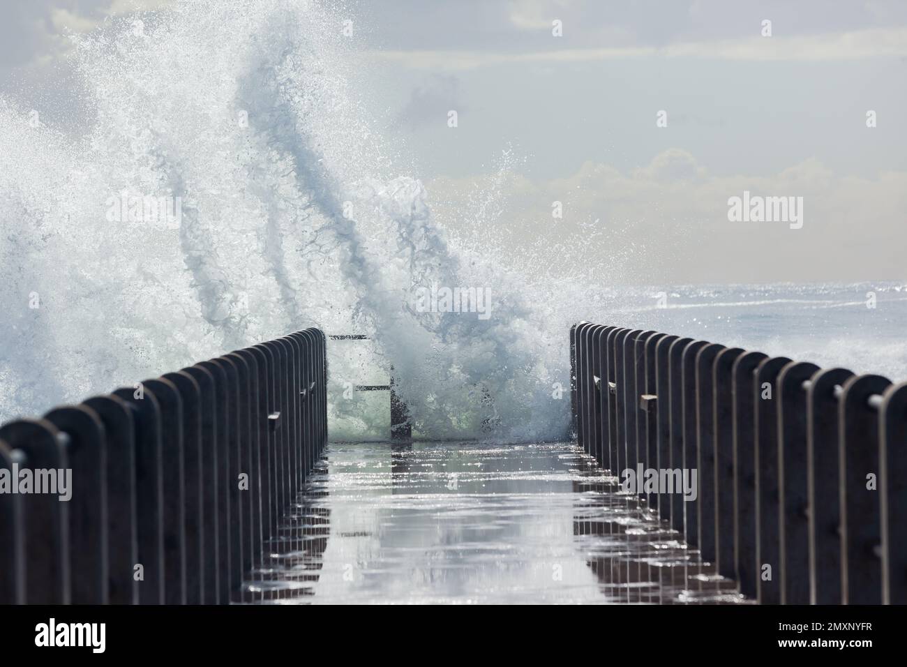 L'acqua dell'oceano che esplode davanti alla piattaforma del molo della spiaggia. Foto Stock