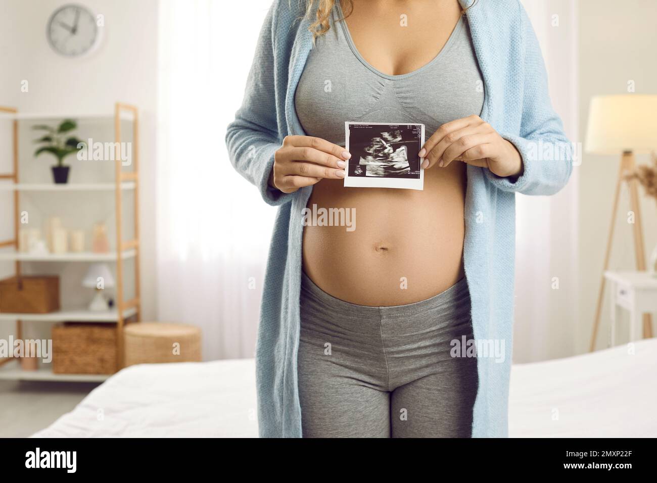 Donna incinta che mostra l'immagine ecografica del feto alla telecamera in piedi a casa in camera da letto. Foto Stock