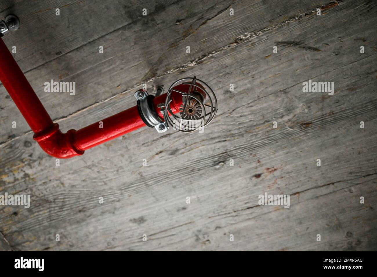 Un particolare di un soffitto rustico con tubi rossi e un allarme antincendio Foto Stock