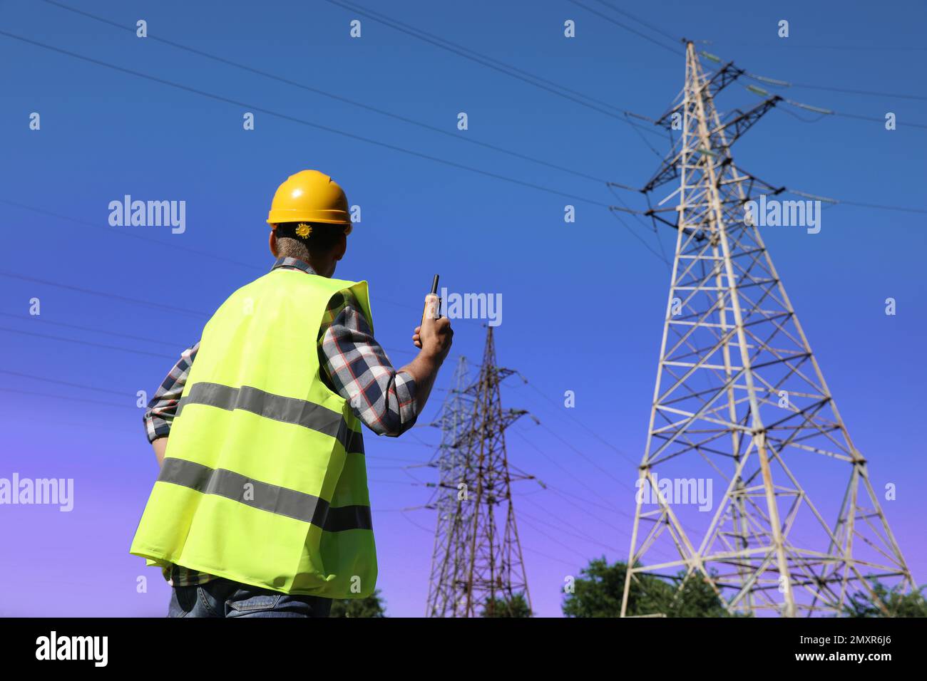 Elettricista professionista con stazione radio portatile vicino alla torre ad alta tensione Foto Stock
