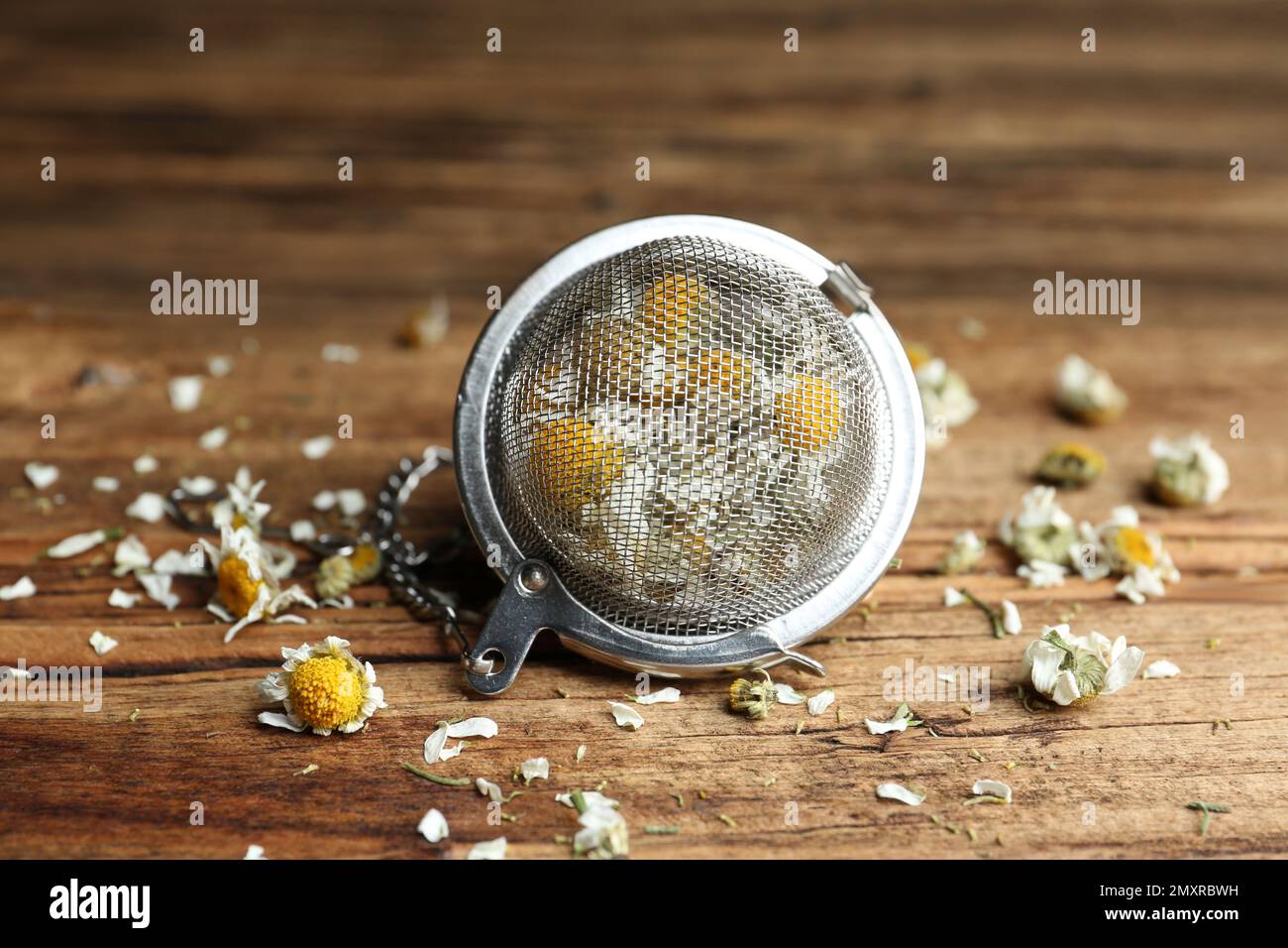 Fiori di camomilla asciutti in infusore su tavolo di legno, primo piano Foto Stock