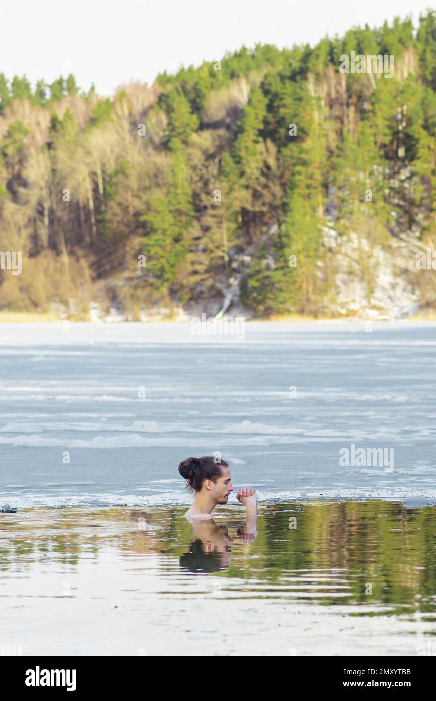 Bel ragazzo o uomo che fa il bagno di ghiaccio nelle acque fredde di un lago. Metodo WIM Hof, terapia fredda, tecniche di respirazione, yoga e meditazione, verticale Foto Stock