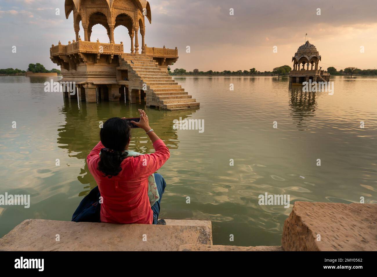 Viaggiatrice indiana, fotografa che fotografa Chhatris e santuari con riflessi sulle acque del lago Gadisar; Jaisalmer. Foto Stock