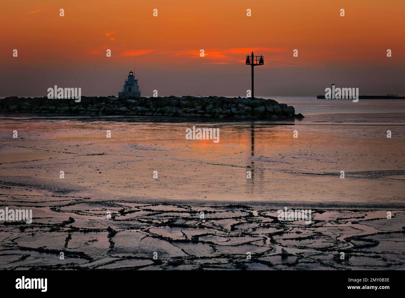 Una colorata alba arancione di gennaio dietro il faro del lago Michigan sul porto ghiacciato di Manitowoc, Wisconsin. Foto Stock