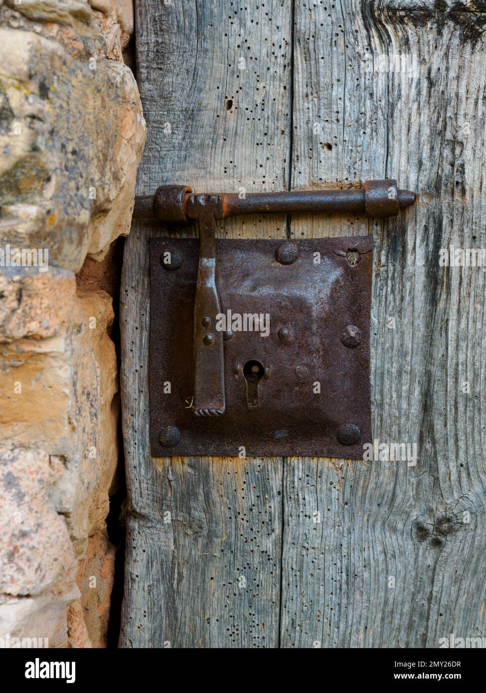 Vecchia serratura di metallo chiusa su porta di legno e fiancheggiata da pietra a sinistra Foto Stock