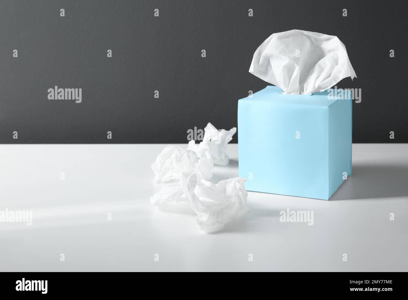 Fazzolettini di carta usati e scatola blu su tavolo bianco. Spazio per il testo Foto Stock