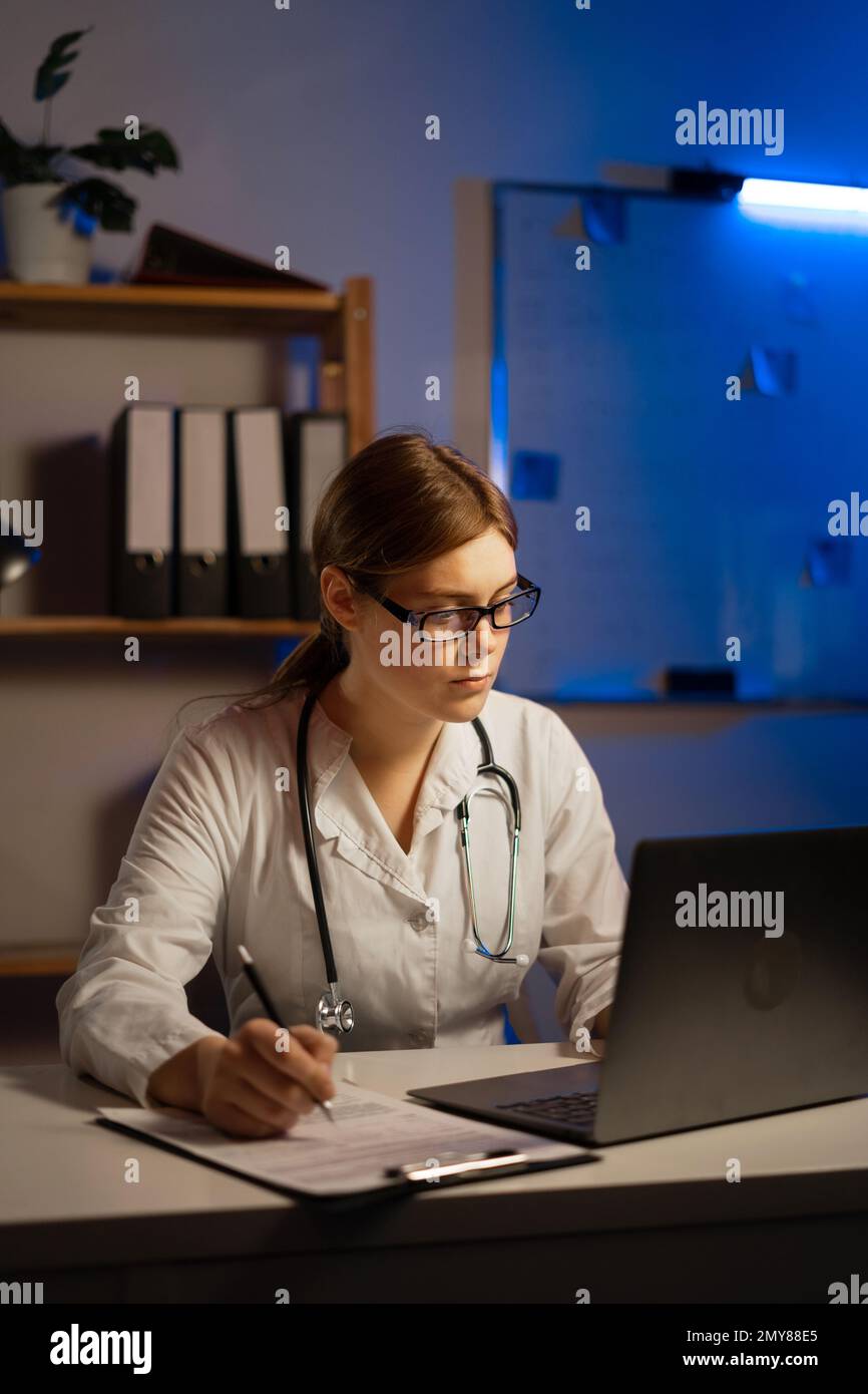 Medico di sesso femminile effettuare una videochiamata online consultare il paziente sul computer portatile mentre si lavora durante il turno di notte. Assistente medico giovane donna terapeuta videoconferenza Foto Stock