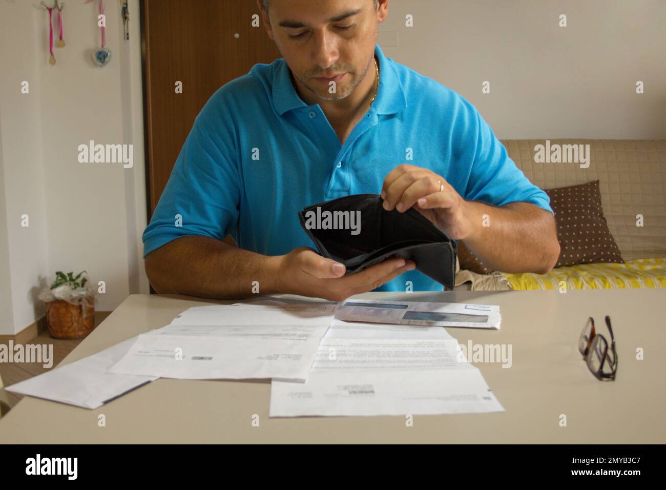 Immagine di un uomo preoccupato con un portafoglio aperto e vuoto in mano mentre controlla le sue fatture di casa che sono appena arrivati. Crisi economica mondiale. Foto Stock