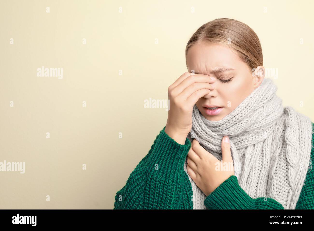 Giovane donna che indossa sciarpa che soffre di mal di testa su sfondo chiaro, spazio per il testo. Sintomi del freddo Foto Stock