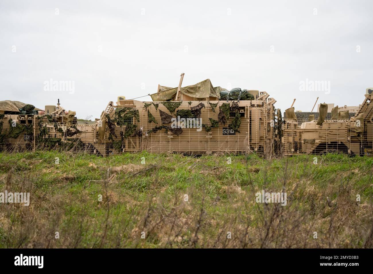 Primo piano di diversi veicoli di pattuglia protetti dall'esercito britannico Mastiff sotto una rete verde di mimetizzazione, Wiltshire UK Foto Stock