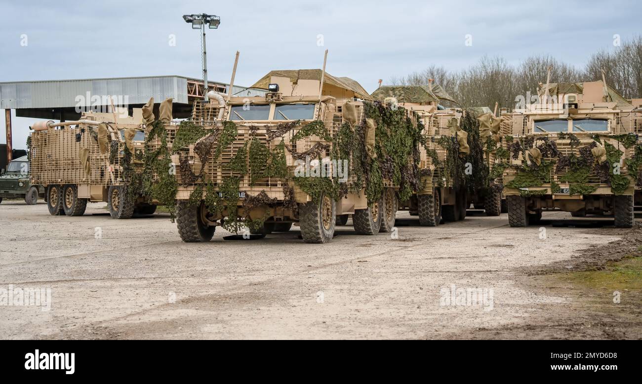 Primo piano di diversi veicoli di pattuglia protetti dall'esercito britannico Mastiff sotto una rete verde di mimetizzazione, Wiltshire UK Foto Stock
