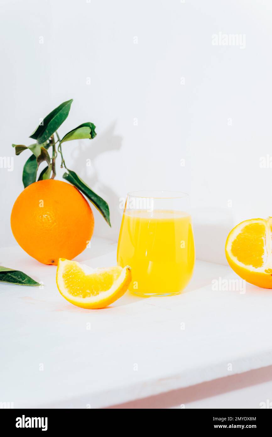 Un bicchiere di succo d'arancia e frutta d'arancia su un tavolo bianco alla luce del sole. Primo piano. Foto Stock