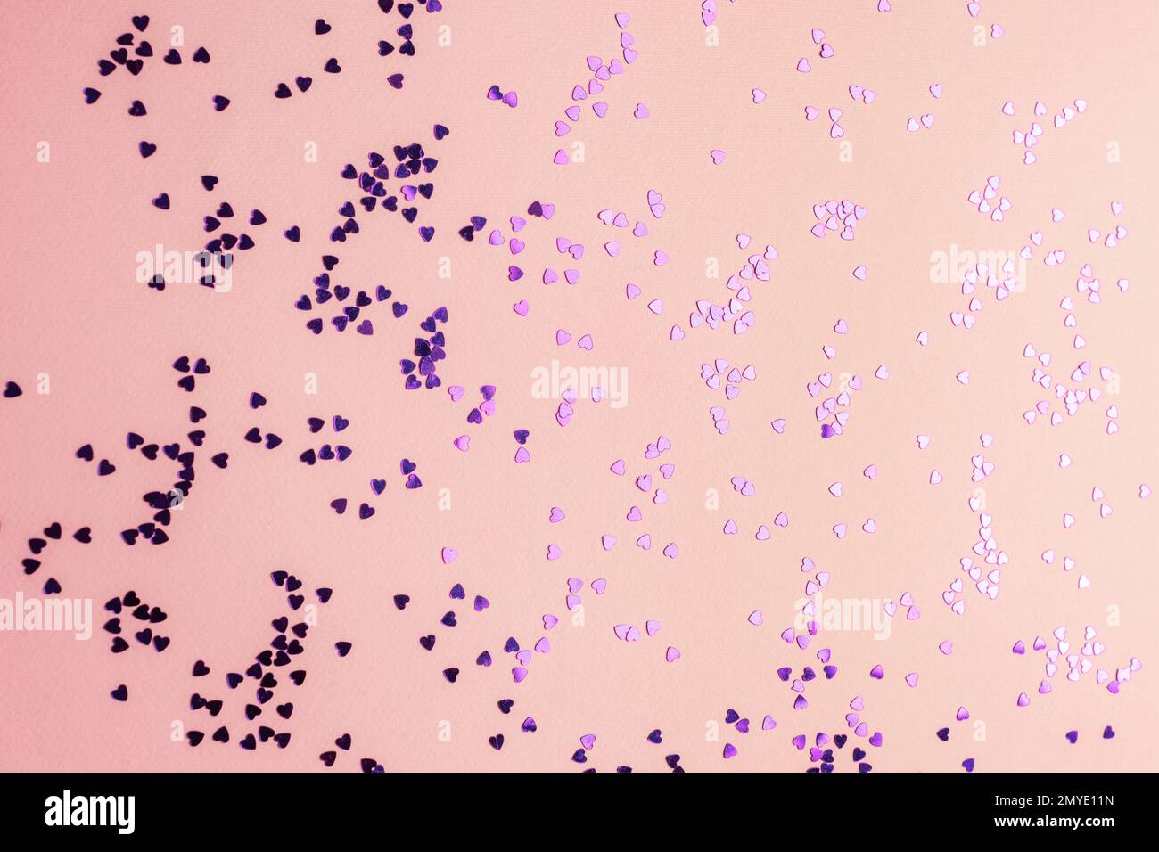 Confetti viola a forma di cuore su sfondo rosa. Foto Stock