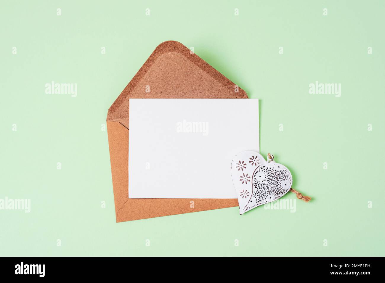 Busta con carta bianca e cuore giocattolo vintage su sfondo verde. Vista dall'alto, piatto, mockup. Foto Stock