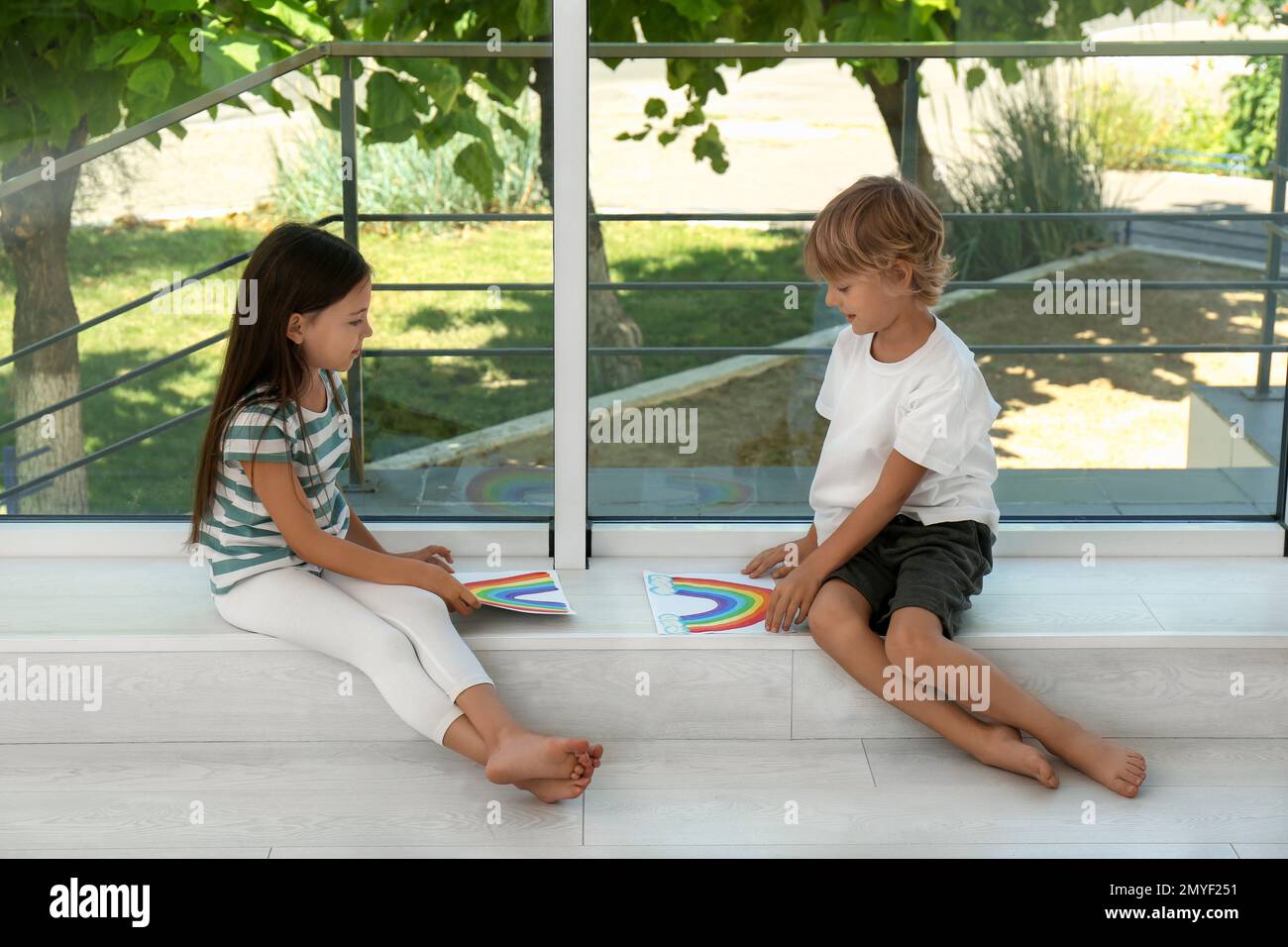 Bambini piccoli con dipinti arcobaleno vicino alla finestra al coperto. Concetto di soggiorno a casa Foto Stock