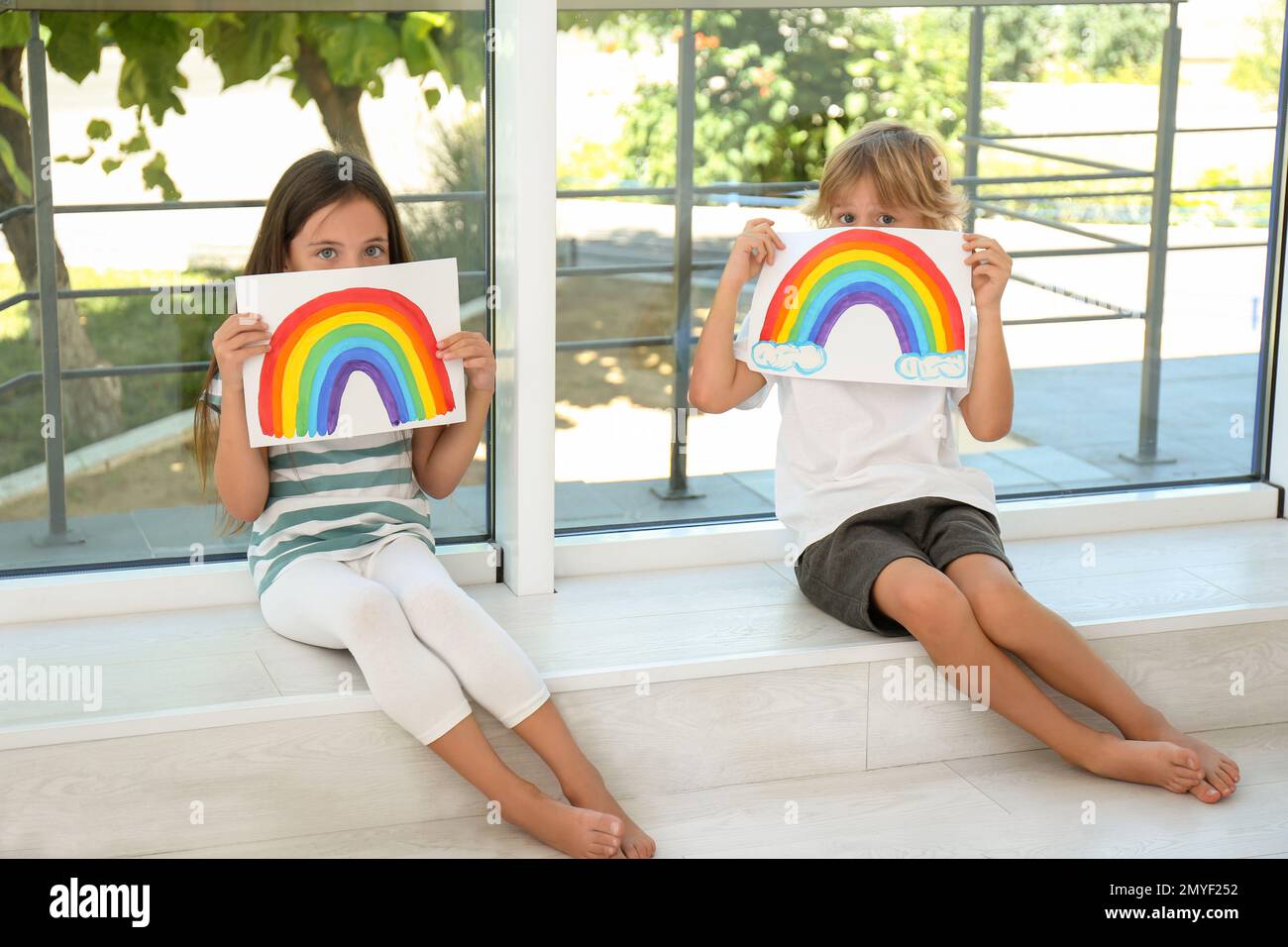 Bambini piccoli che tengono dipinti arcobaleno vicino alla finestra al coperto. Concetto di soggiorno a casa Foto Stock