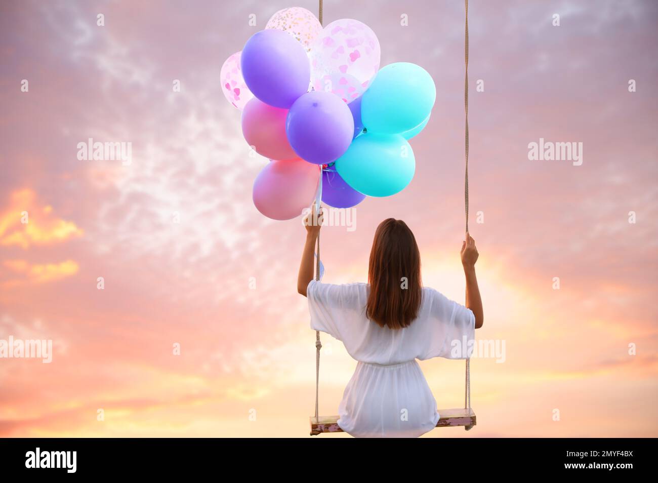 Il mondo dei sogni. Giovane donna con palloncini luminosi che oscillano, cielo tramonto sullo sfondo Foto Stock